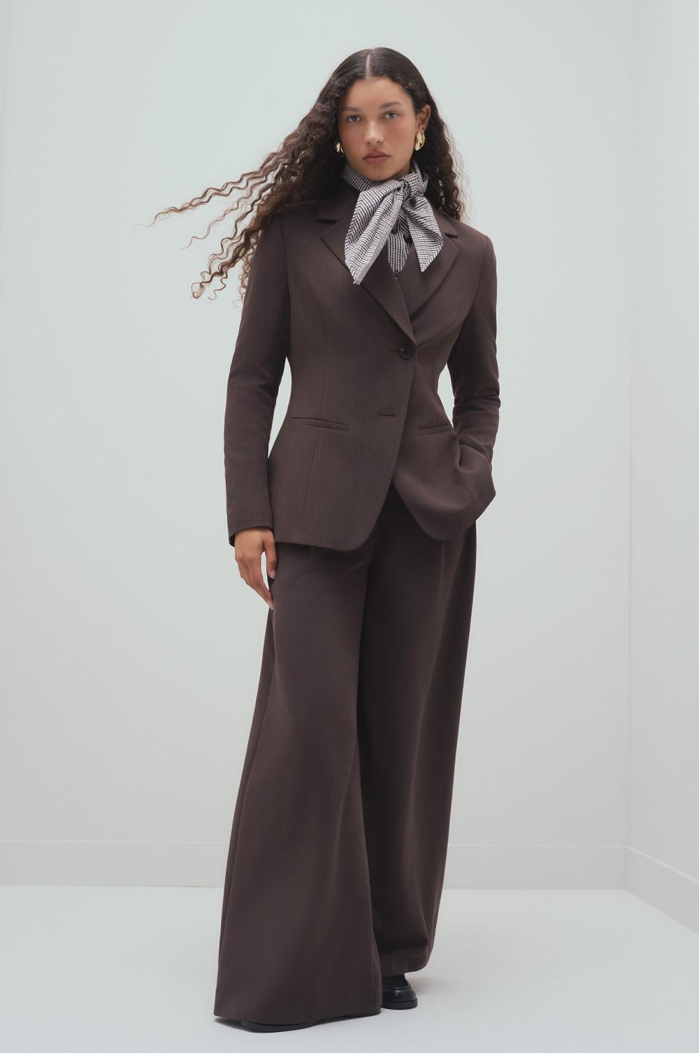Model wearing brown tailored blazer and wide-leg pants with checked neck scarf and gold hoop earrings.