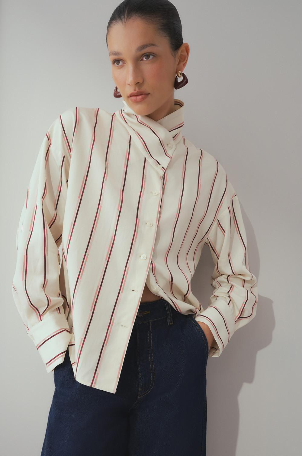 Model wearing cream shirt with red vertical stripes and dark denim pants, styled with brown earrings.