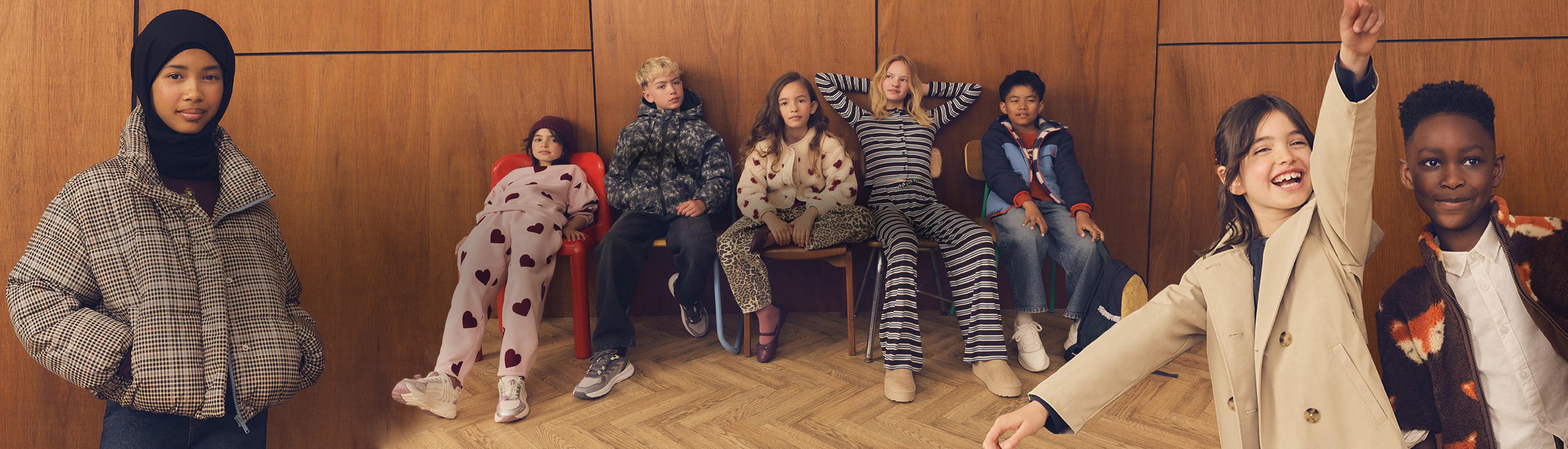 Group of diverse children wearing casual winter clothing and patterned loungewear sitting and posing together.