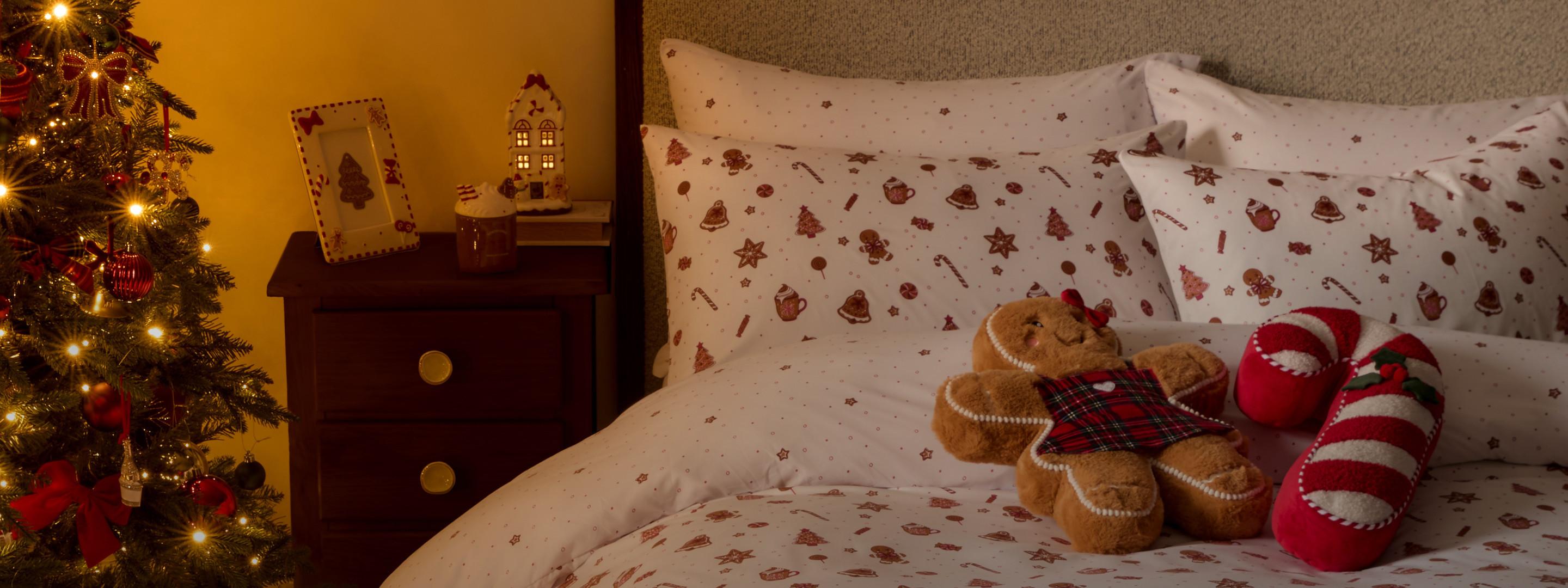 Dormitorio con decoración navideña, que incluye un árbol de Navidad, ropa de cama con diseños de temporada y un cojín con forma de galleta de jengibre sobre la cama.