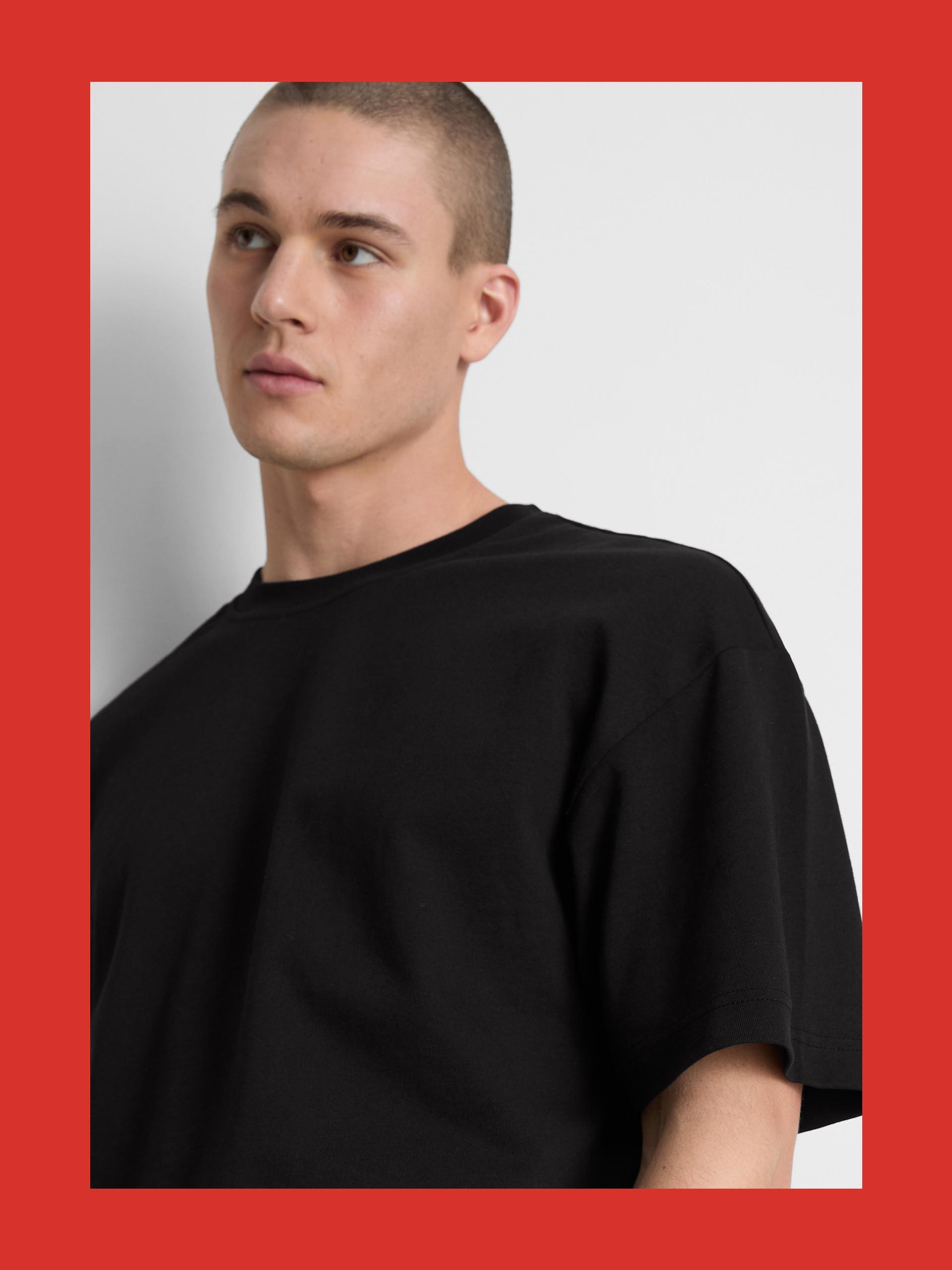 Person wearing a plain black oversized t-shirt against a neutral background with red border.