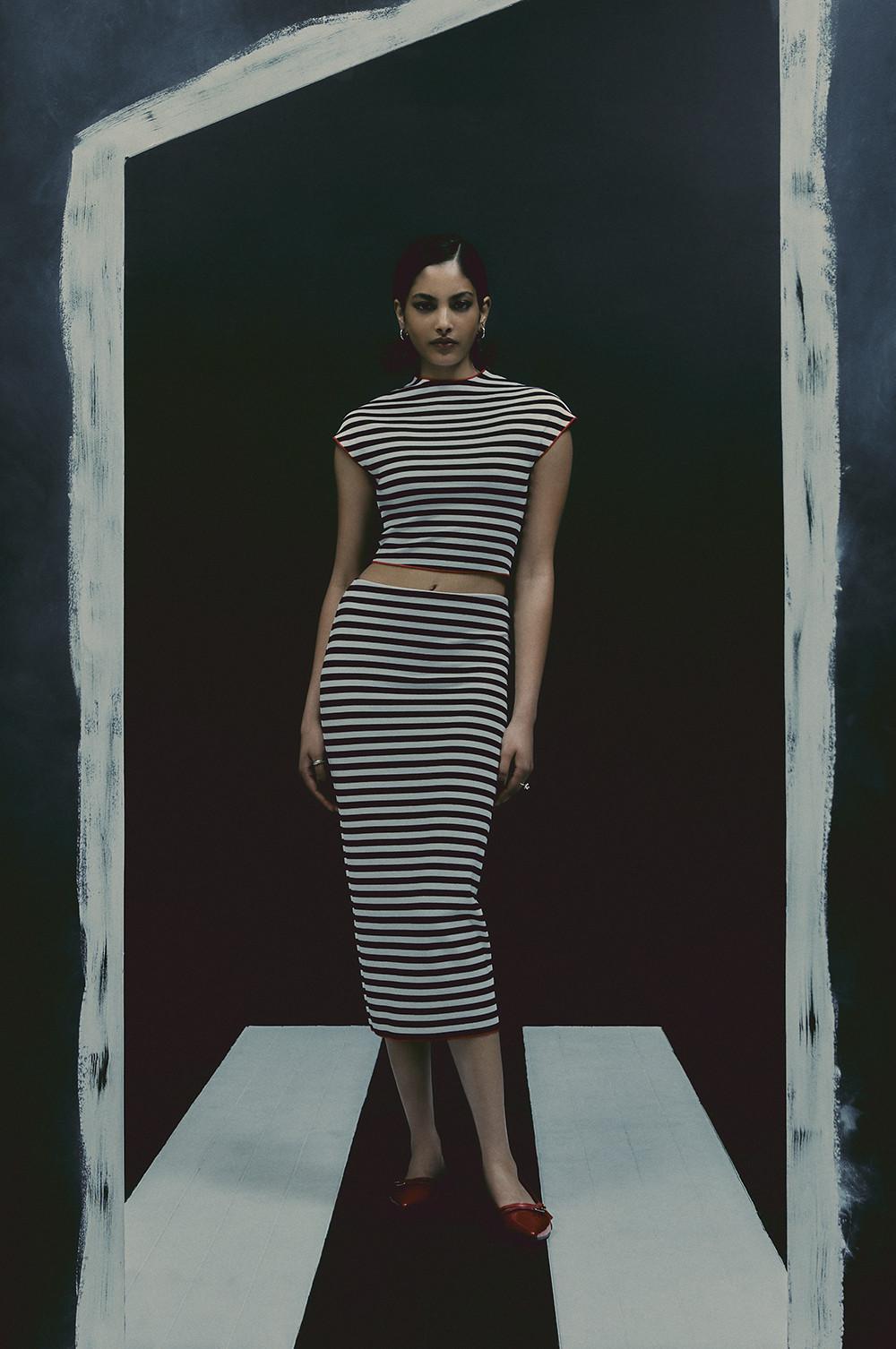 Le mannequin porte une jupe mi-longue à rayures noires et blanches et un haut court assorti