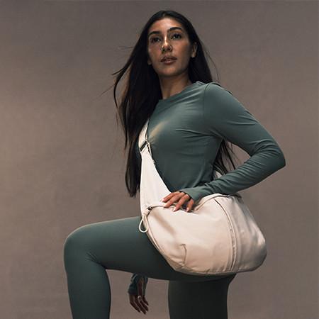Person wearing teal athletic wear with a cream crossbody bag against a neutral backdrop.