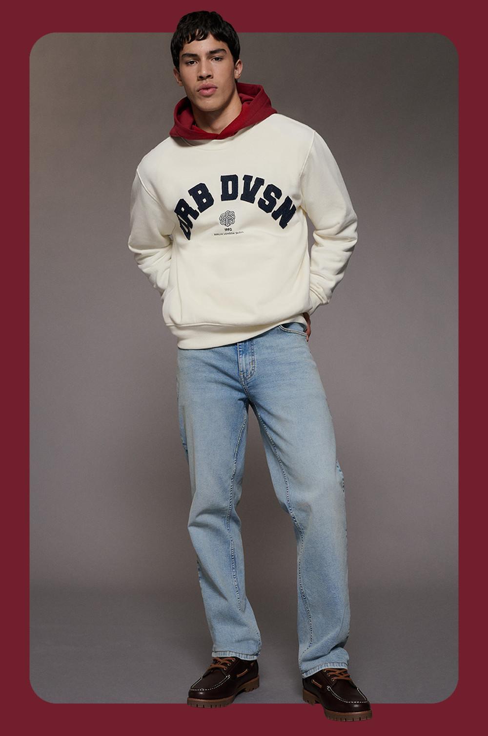 model wearing cream sweatshirt with RB DVSN text, red hoodie underneath, and light blue jeans.