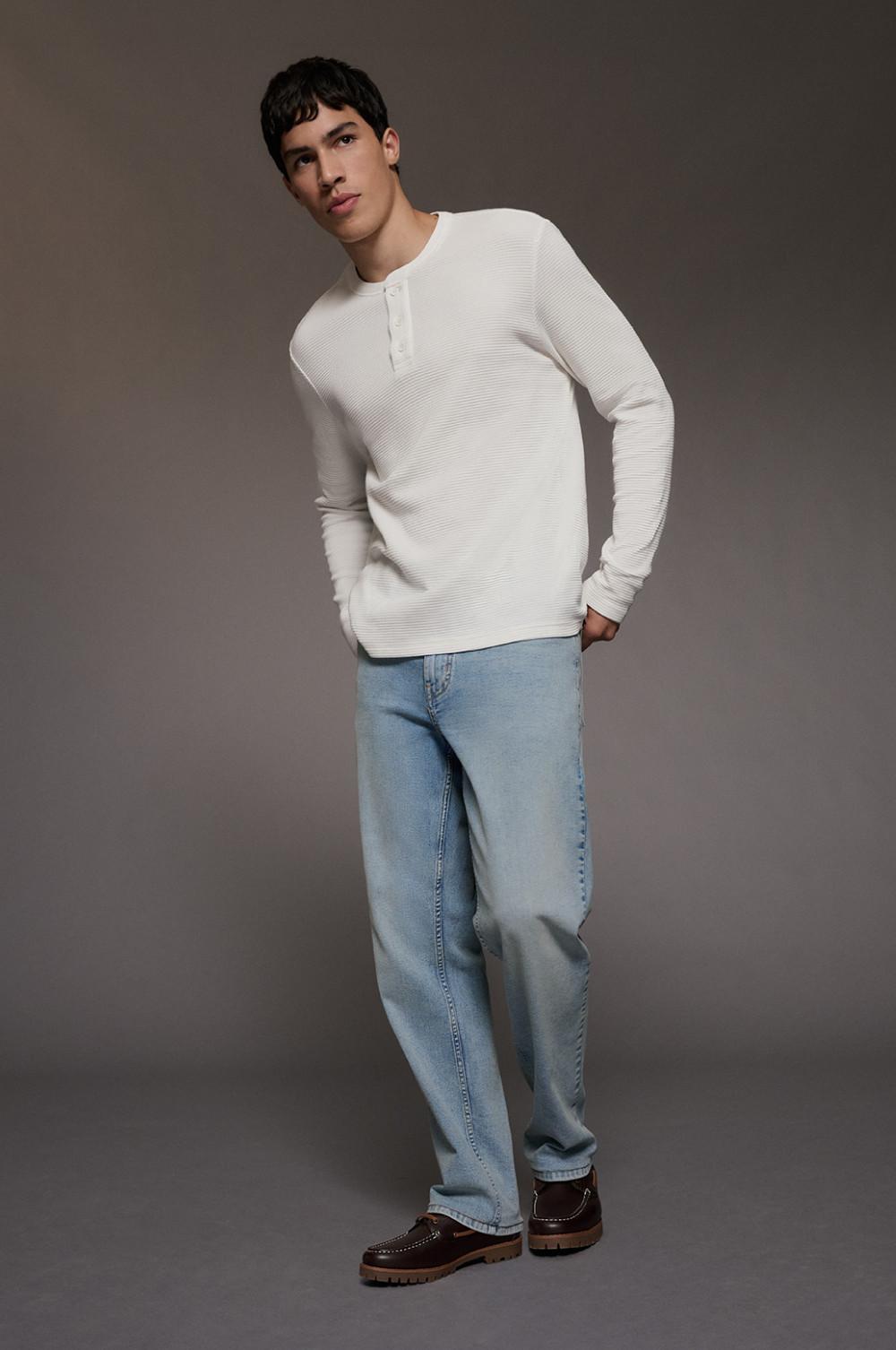 model wearing cream textured henley top with light blue jeans and brown suede shoes.