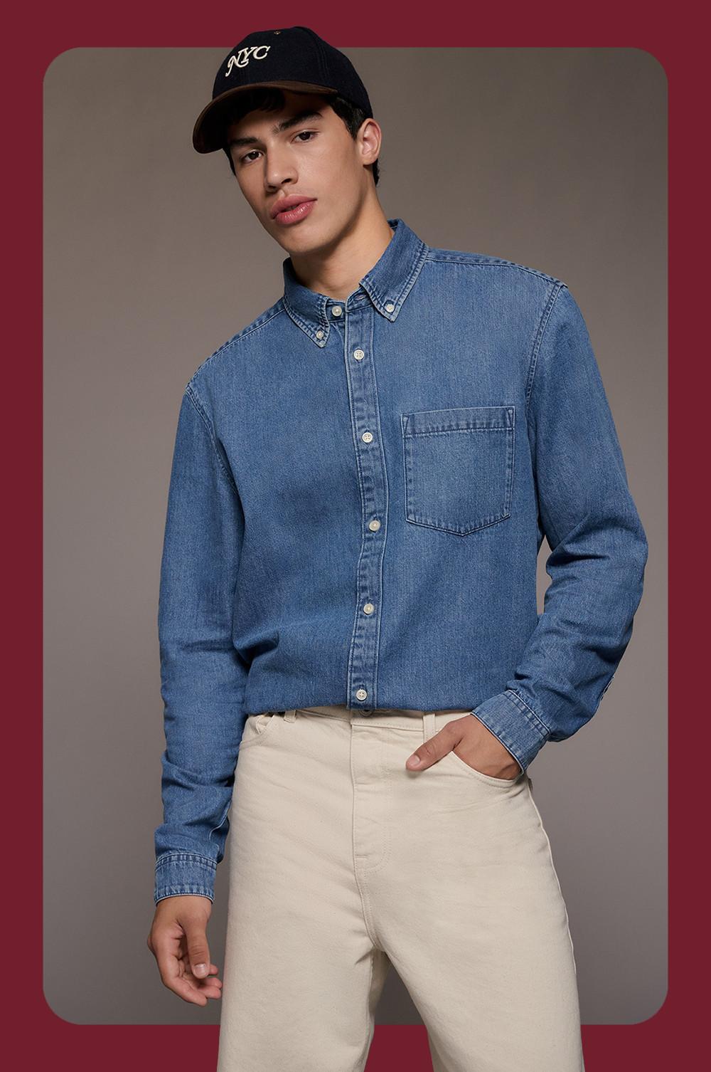 model wearing blue denim shirt with chest pocket and beige pants, styled with black NYC baseball cap.