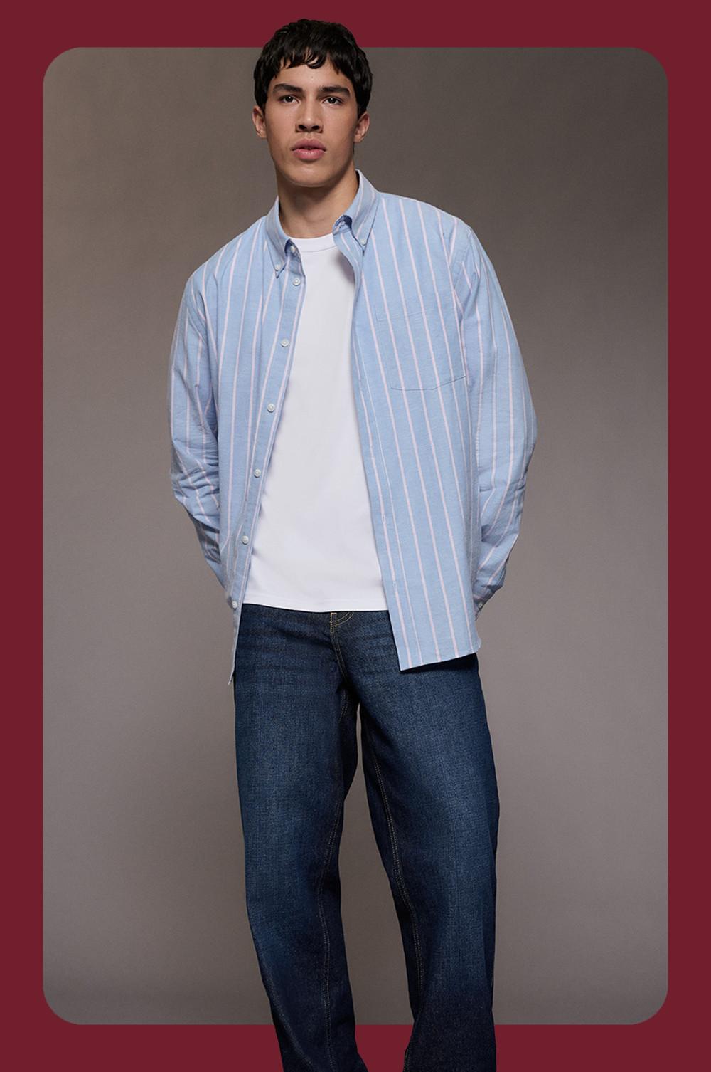 model wearing light blue vertical striped shirt over white T-shirt with dark blue jeans.
