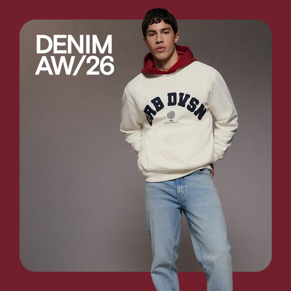 Model wearing cream sweatshirt with JRB DVSN text and red hood, paired with light blue denim jeans.