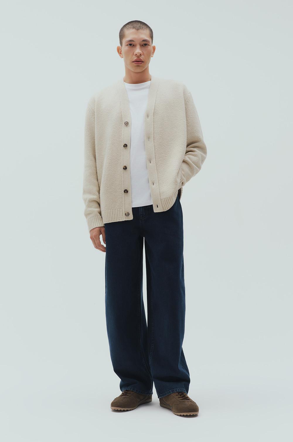 Model wearing a beige button-up cardigan over a white T-shirt with navy wide-leg pants and brown shoes.