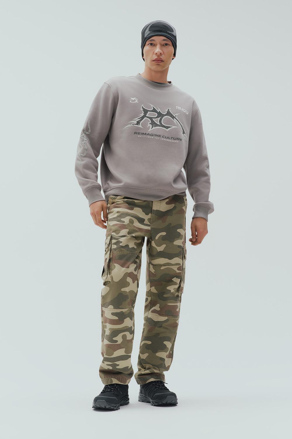 Model wearing gray graphic sweatshirt with camouflage cargo pants and black beanie.