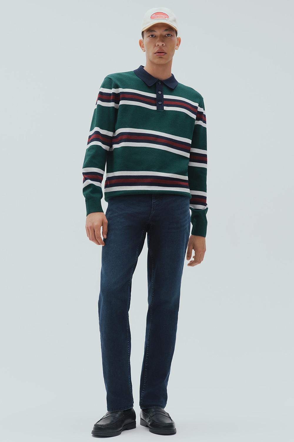 Model wearing green striped long-sleeve polo shirt with navy collar, dark blue jeans and white cap.