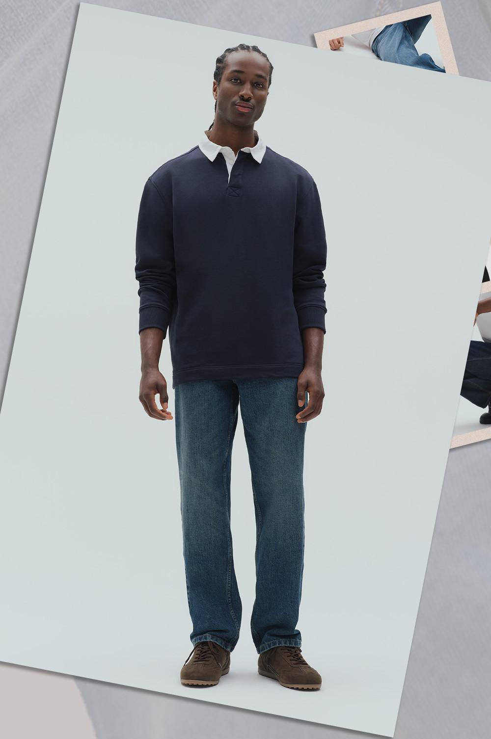 Model wearing navy rugby shirt with white collar and blue jeans, standing with hands at sides.