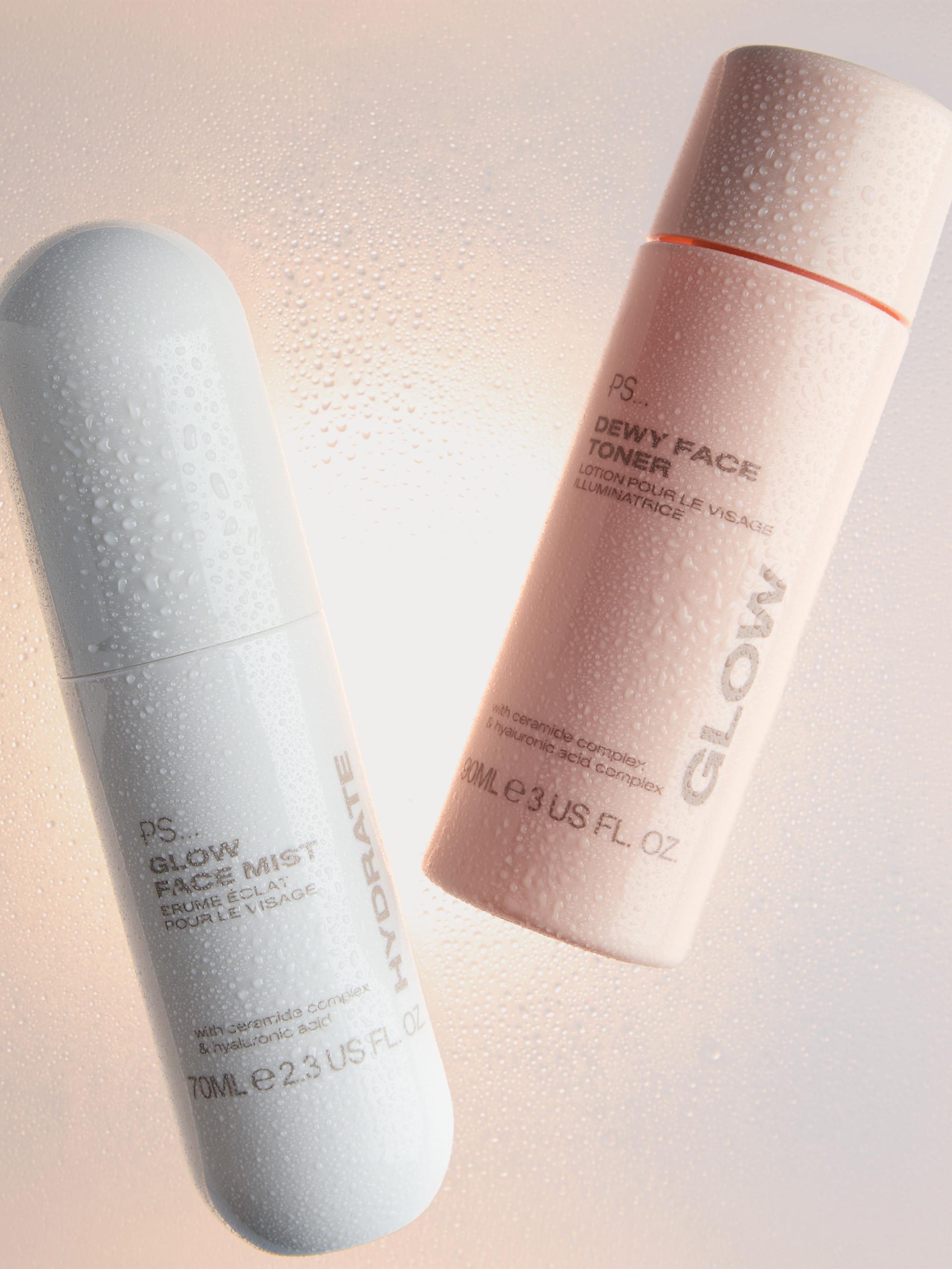 Three PS Cooling body mist bottles in orange, pink and green with water droplets on glass shelf.