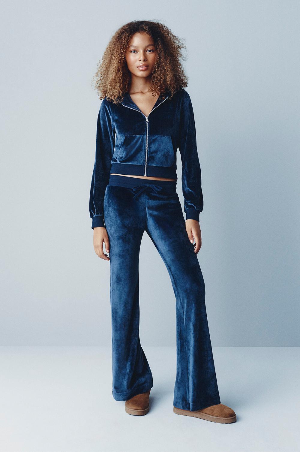 Model wearing navy blue velour tracksuit with zip-up hoodie and flared pants, paired with tan boots.