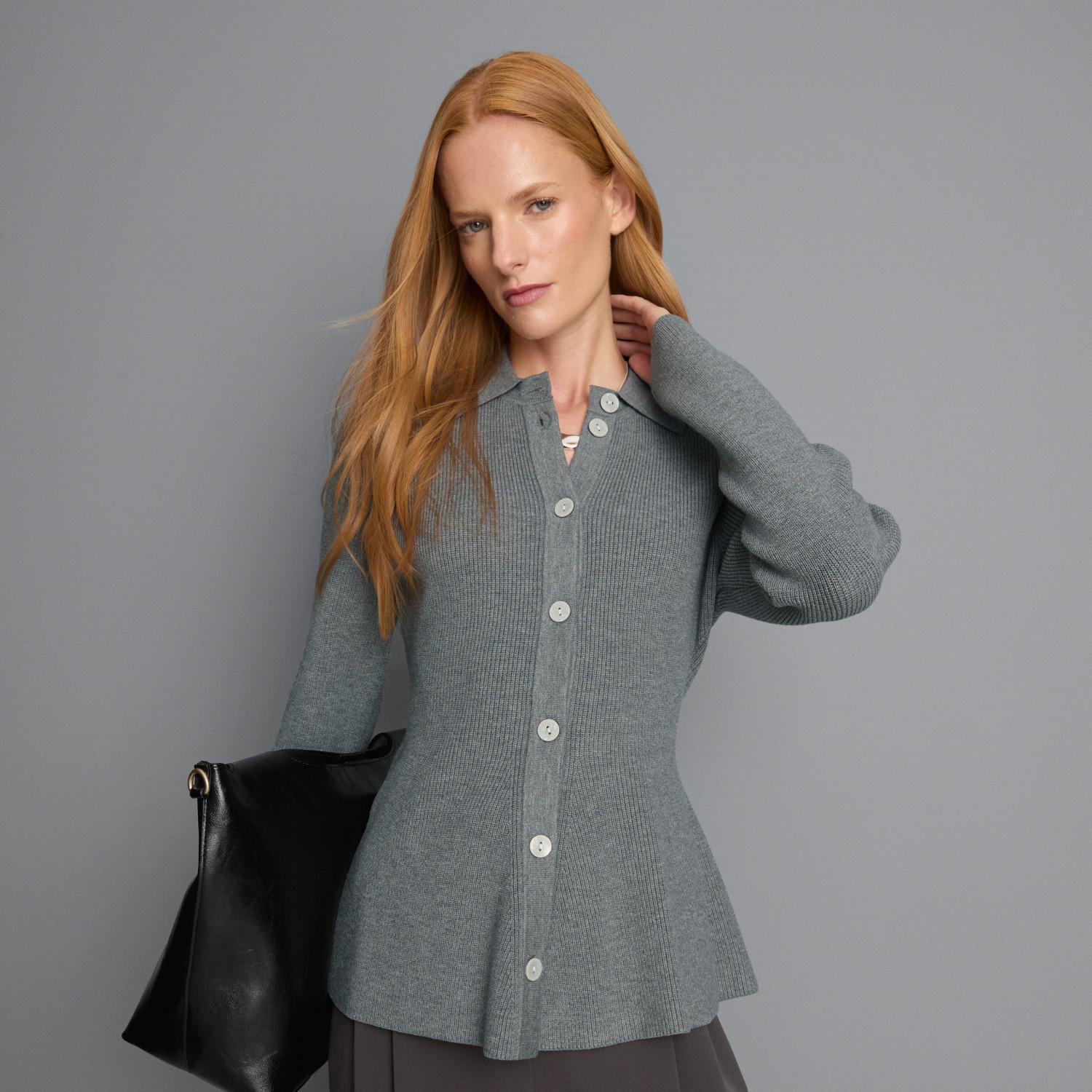 Woman wearing gray ribbed button-front cardigan with hand touching hair, holding black leather bag.