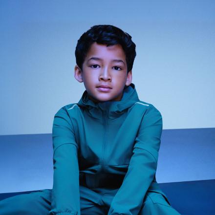 Young boy wearing a teal hooded jacket, sitting and looking directly at the camera.