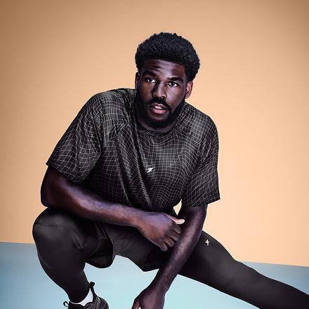 Man crouching wearing olive green checked t-shirt and black trousers.