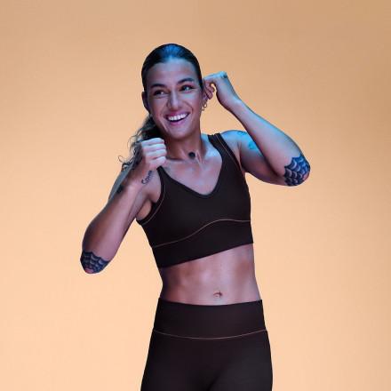 Woman wearing black sports bra and leggings, smiling whilst holding a water bottle.
