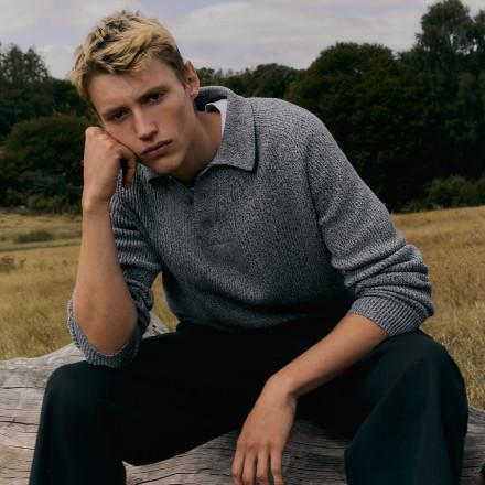 Man crouching wearing olive green checked t-shirt and black trousers.