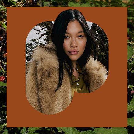 Woman wearing a luxurious faux fur collar jacket with hood, styled in a circular frame composition.