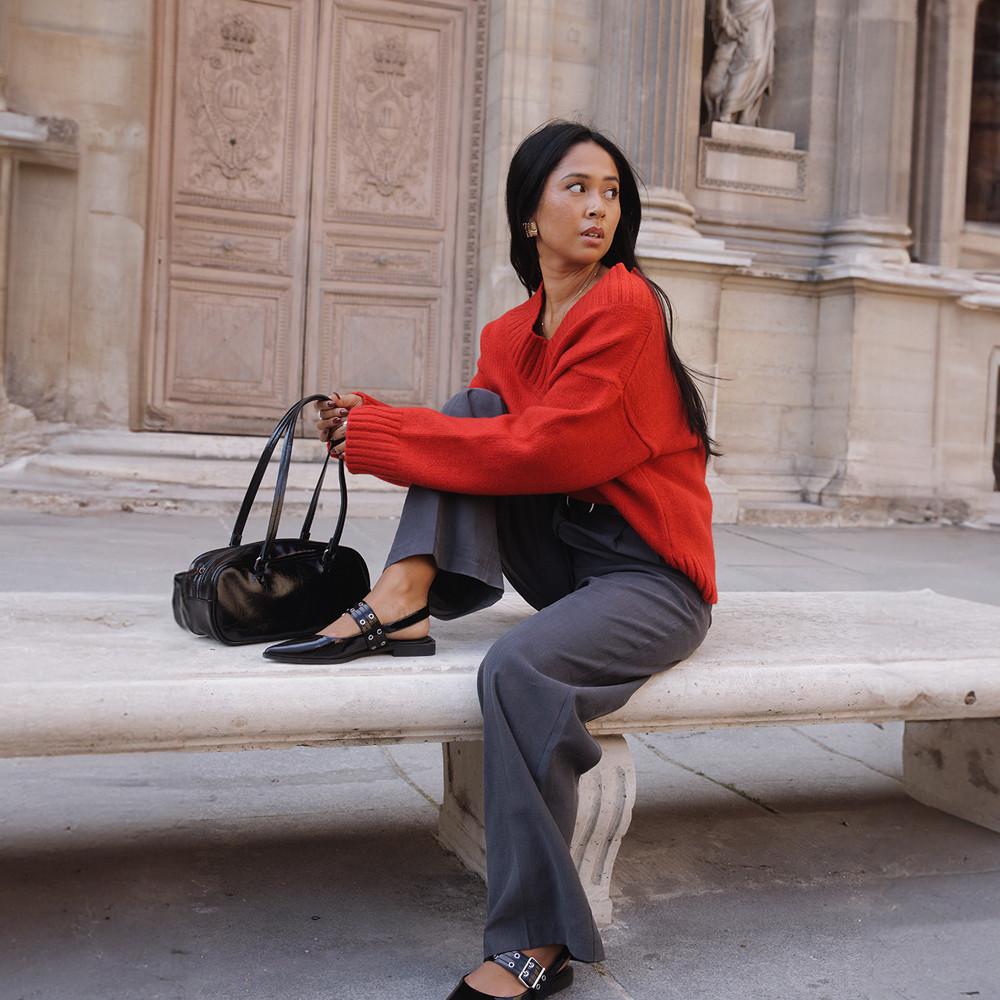 Model wears red jumper, grey trouser, black flats and a black bag
