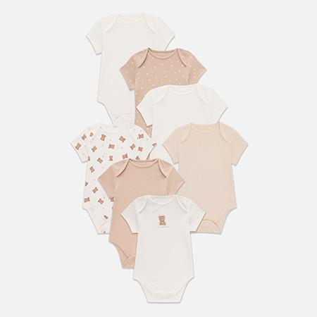Seven baby bodysuits in cream and beige tones with short sleeves, including patterns with dots and teddy bears.