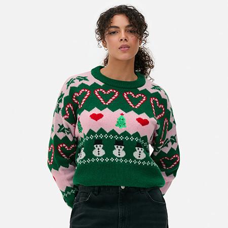 Green festive jumper with candy cane hearts, Christmas trees and snowmen pattern on pink background.