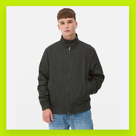 Person wearing a dark grey zip-up jacket with stand collar and blue jeans against white background.