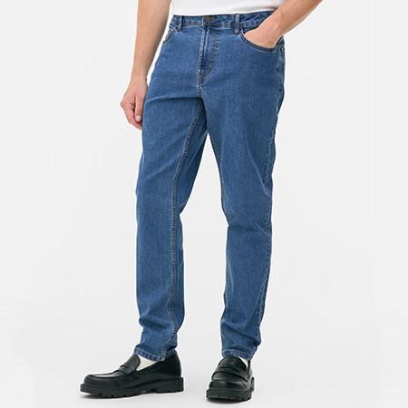 Person wearing medium wash straight-leg jeans with hand in pocket, paired with black loafers.