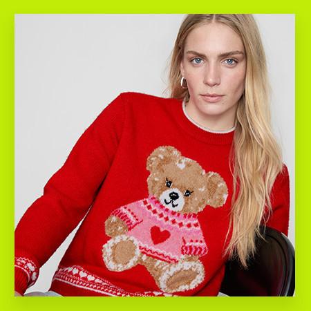 Bright red jumper featuring a teddy bear design wearing a pink patterned sweater with heart detail.