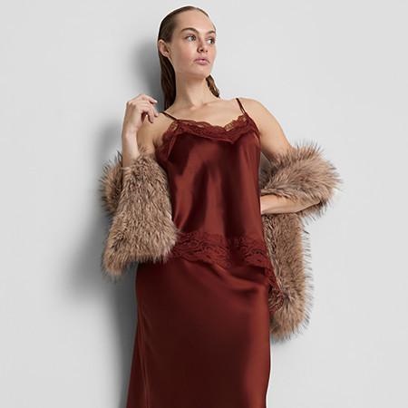 Woman wearing burgundy satin slip dress with lace detail, draped with fluffy brown faux fur wrap.
