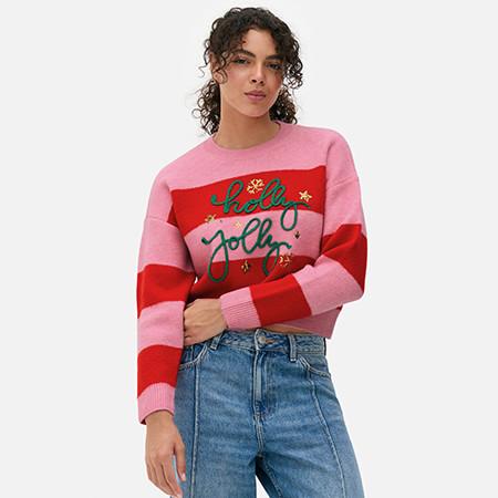 Person wearing a pink and red striped jumper with "Holly Jolly" text, paired with blue denim jeans.
