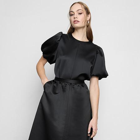 Person wearing an elegant black dress with puffed short sleeves and a gathered waist.