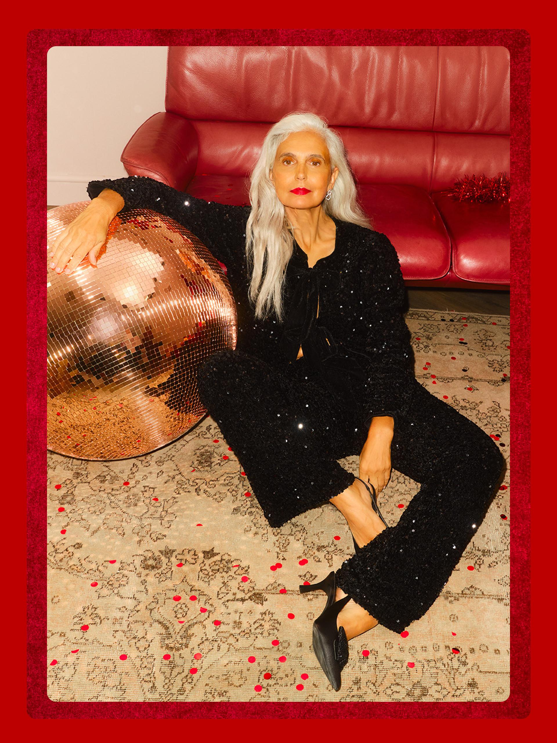 Person wearing sparkling black outfit sitting on red leather sofa with copper disco ball on patterned rug.