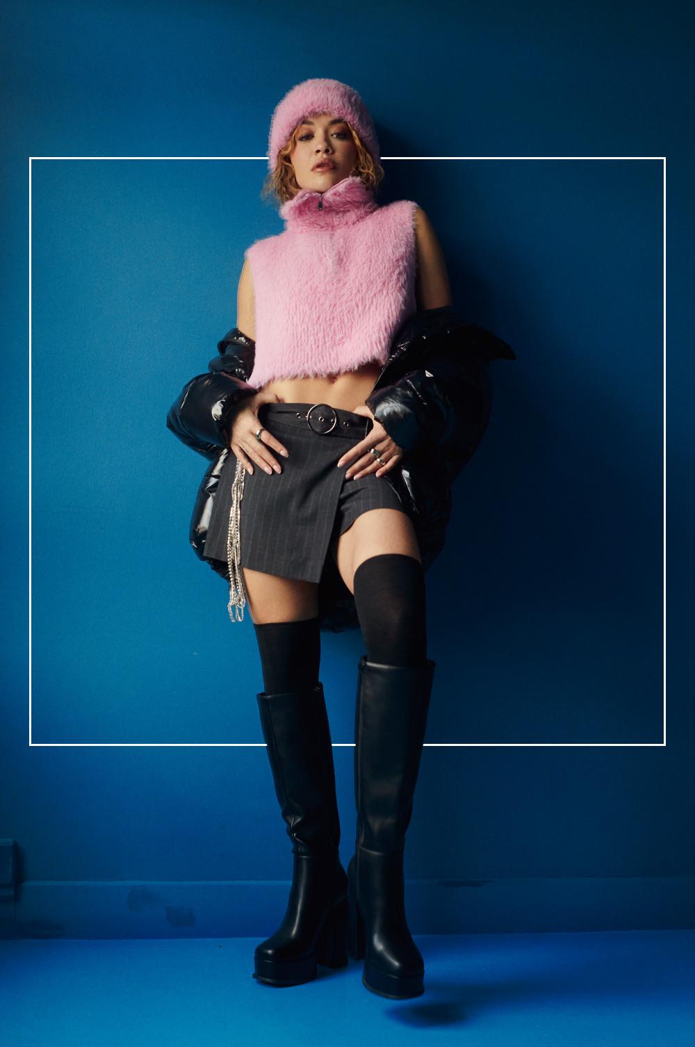 Model wears pinstriped mini skirt, pink faux fur bib with matching pink hat and thigh high boots