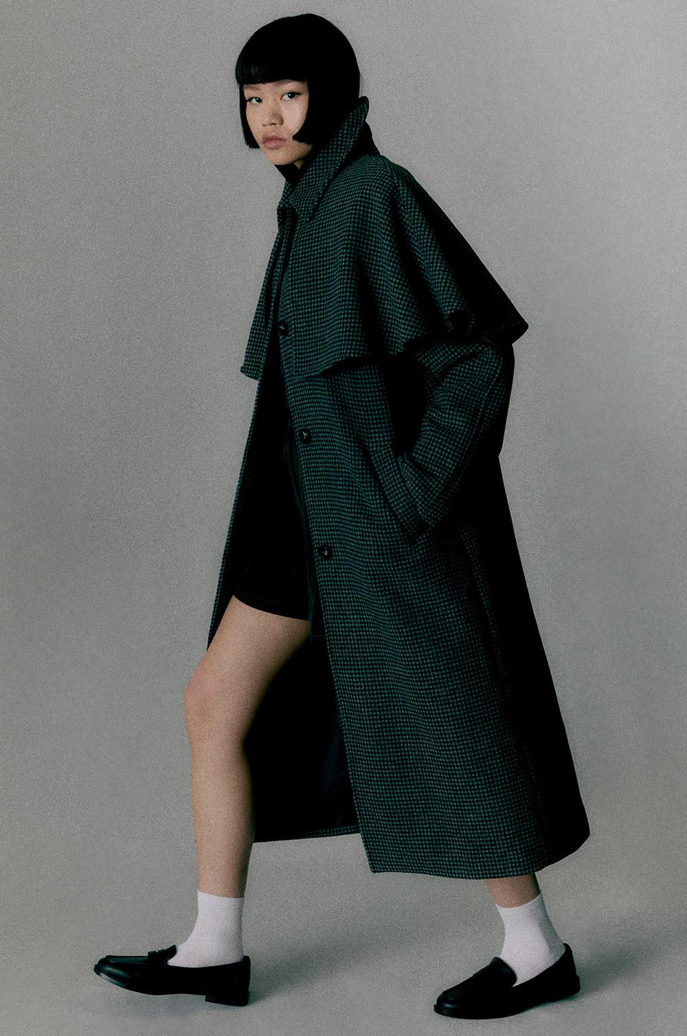Cappotto a quadri verde scuro e nero indossato con un abito corto, calzini bianchi e mocassini neri.