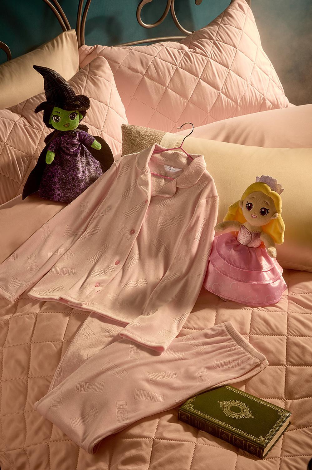 Pink pyjama set on quilted bedding with witch and princess plush toys and a vintage book.
