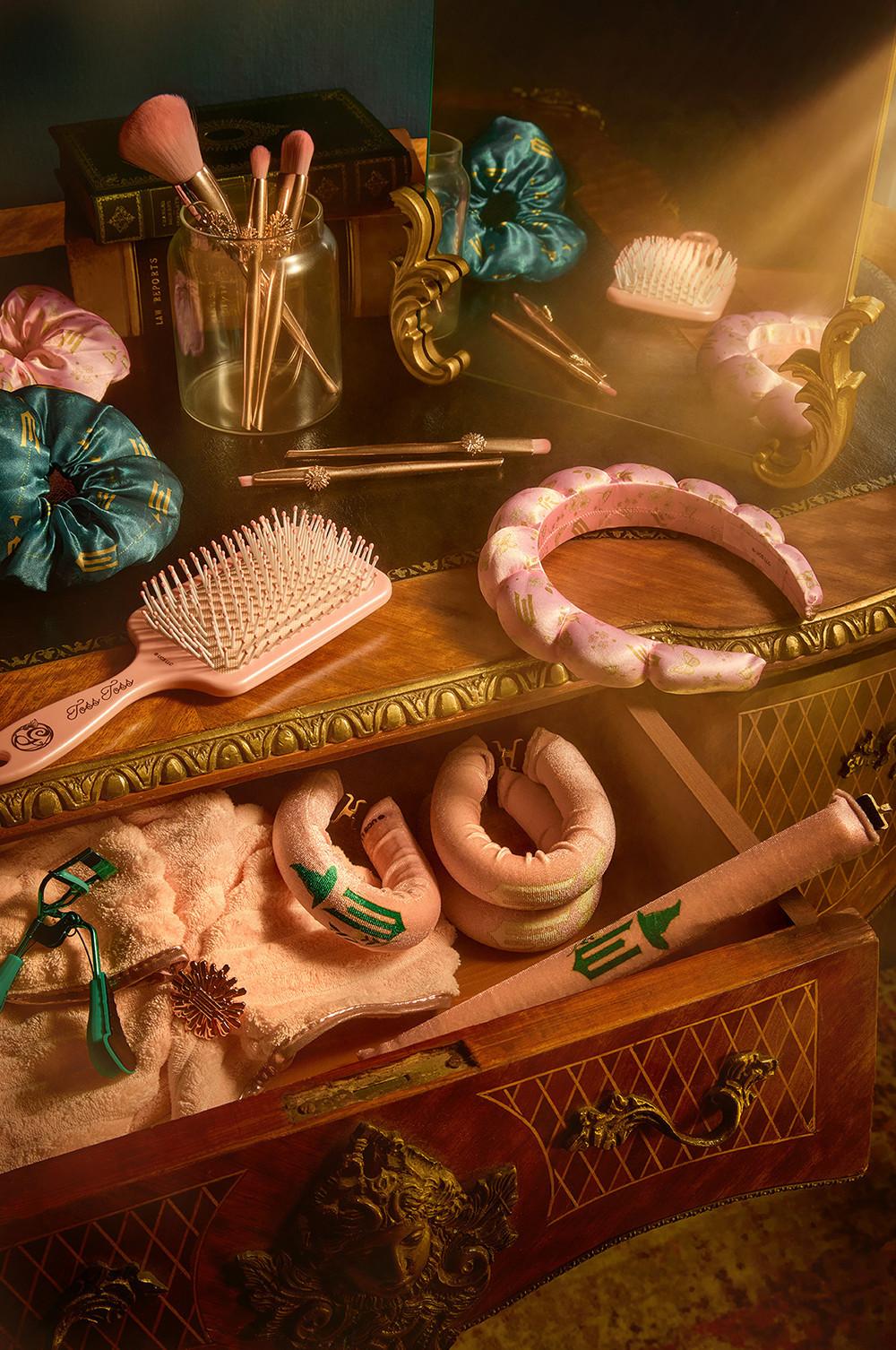 Vanity setup with makeup brushes, hair scrunchies, pink hairbrush, and towels arranged on an ornate wooden dresser.