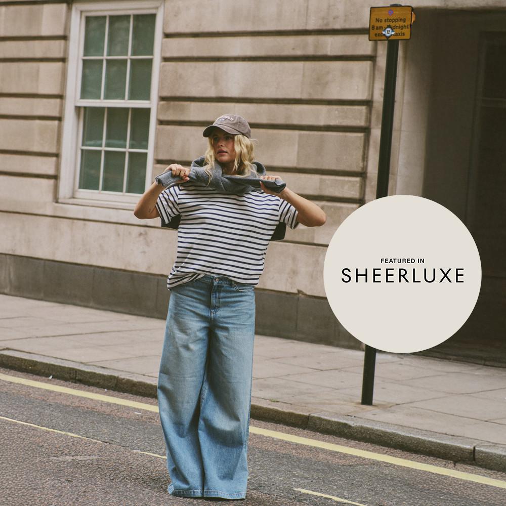 Person wearing striped t-shirt, wide-leg jeans and cap on city street, featured in Sheerluxe.