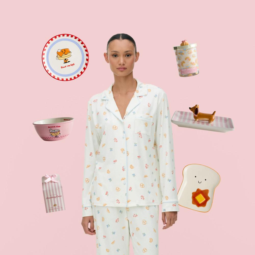 Person wearing white patterned pyjamas surrounded by breakfast-themed homeware including plates, bowls and ornaments.