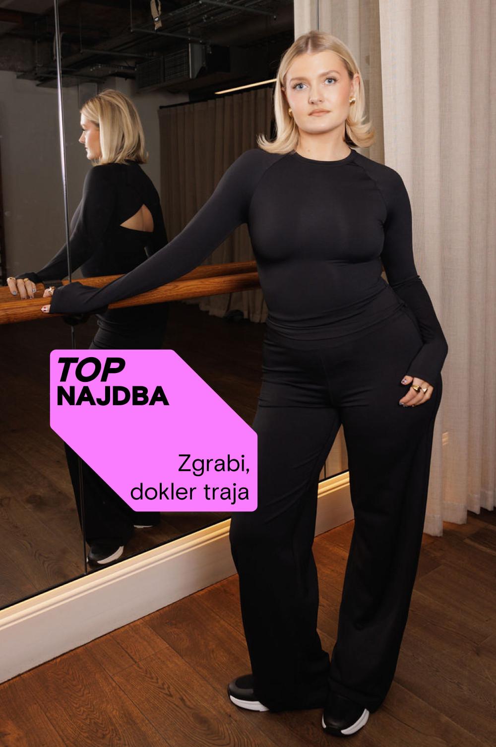 Oseba v oprijetem črnem zgornjem delu z dolgimi rokavi in hlačah poleg ogledala z rožnato promocijsko oznako »MAJOR FIND«.