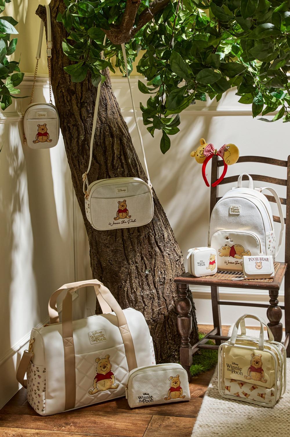 Collection of Disney Winnie the Pooh bags and accessories displayed around a tree trunk, including backpack, crossbody bags and headband.