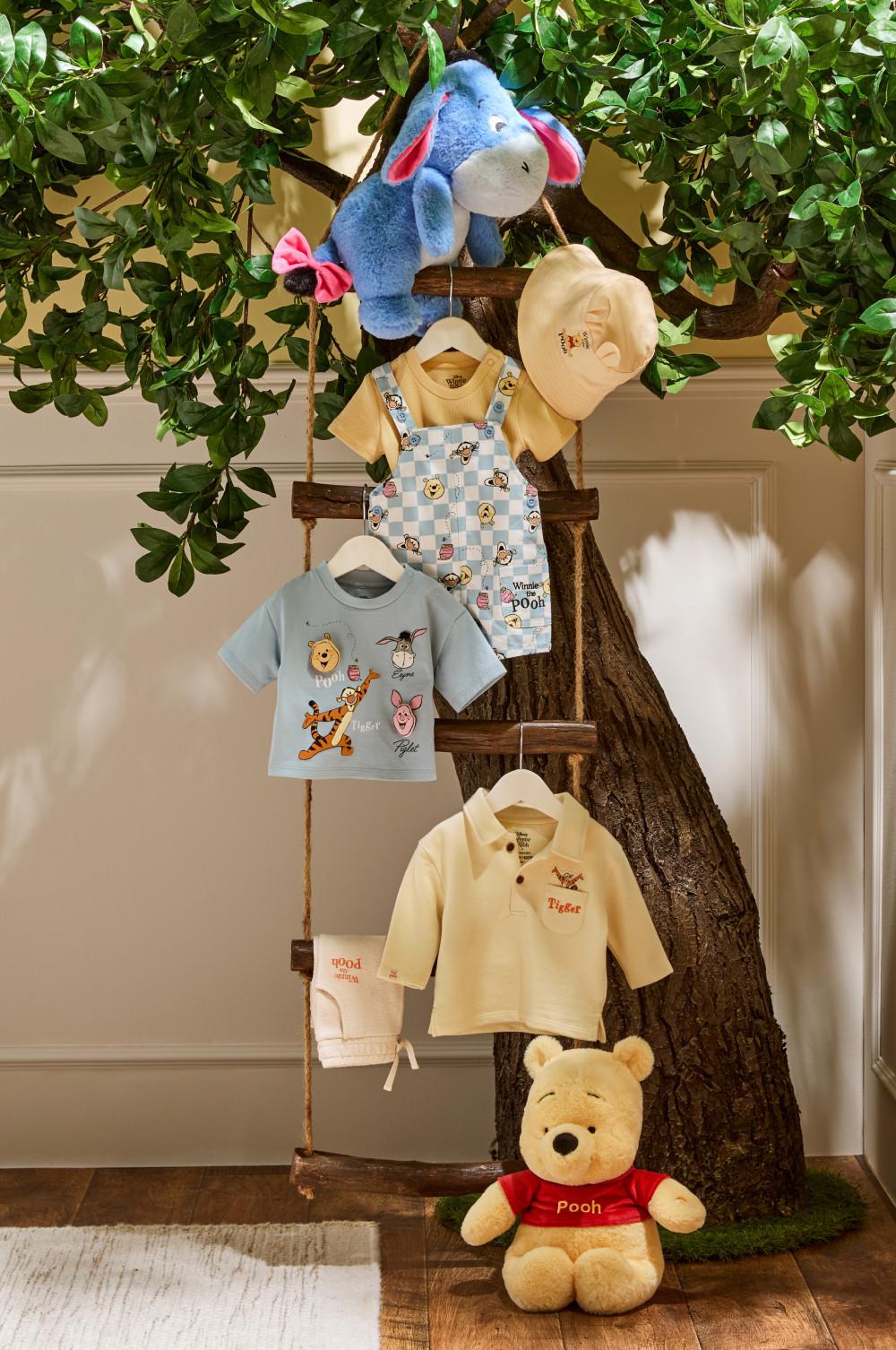 Winnie the Pooh children's clothing collection displayed on tree-shaped stand with Pooh and Eeyore soft toys.