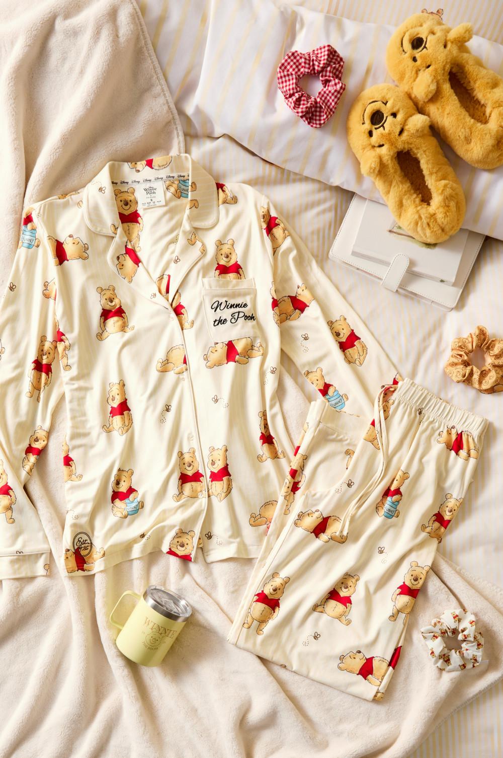 Winnie the Pooh pyjama set with matching slippers, hair scrunchies and candle on a bed.
