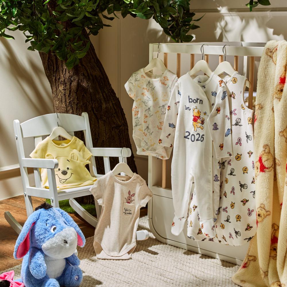 Disney Winnie the Pooh baby clothing collection displayed on nursery furniture with Eeyore plush toy.