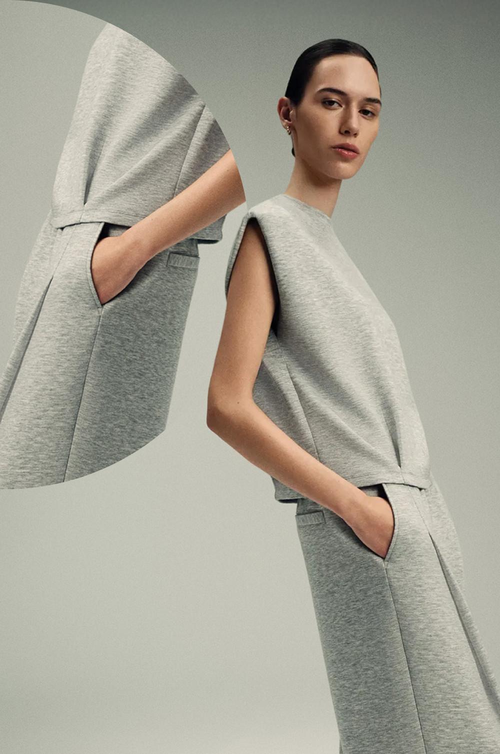 Modelo con ropa para estar en casa sin mangas de color gris, con las manos en los bolsillos, sobre un fondo de color neutro.
