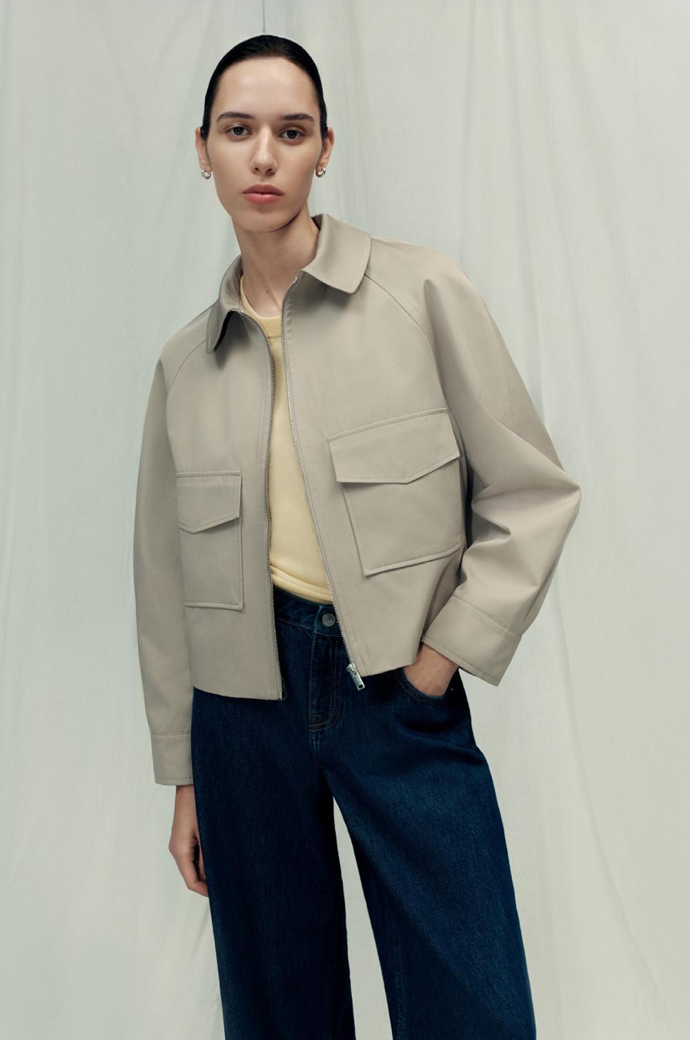 Chaqueta corta beis con bolsillos delanteros sobre un top amarillo y vaqueros azules sobre un fondo de color neutro.