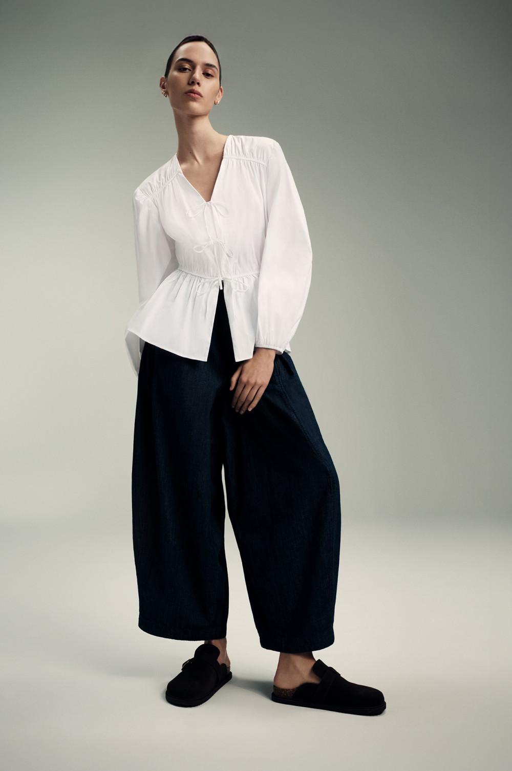 Blusa blanca con péplum y cordón de ajuste en la cintura, pantalón azul marino de pernera ancha y mocasines negros.