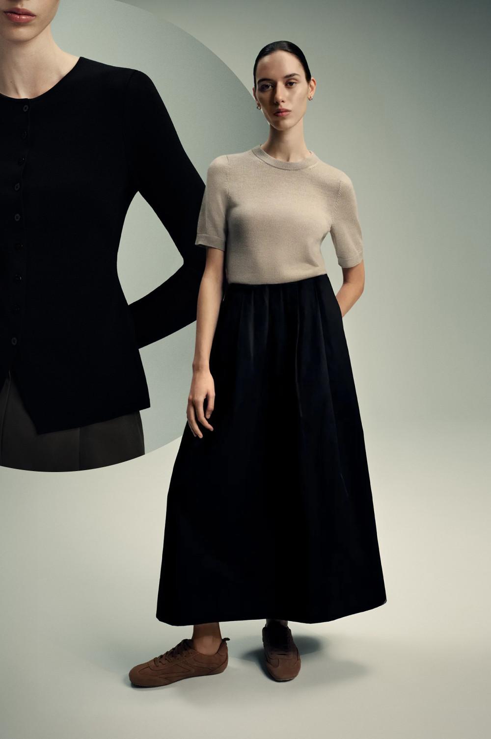 Conjunto minimalista con top de punto beis y manga corta, falda larga negra y zapatillas de ante marrones.