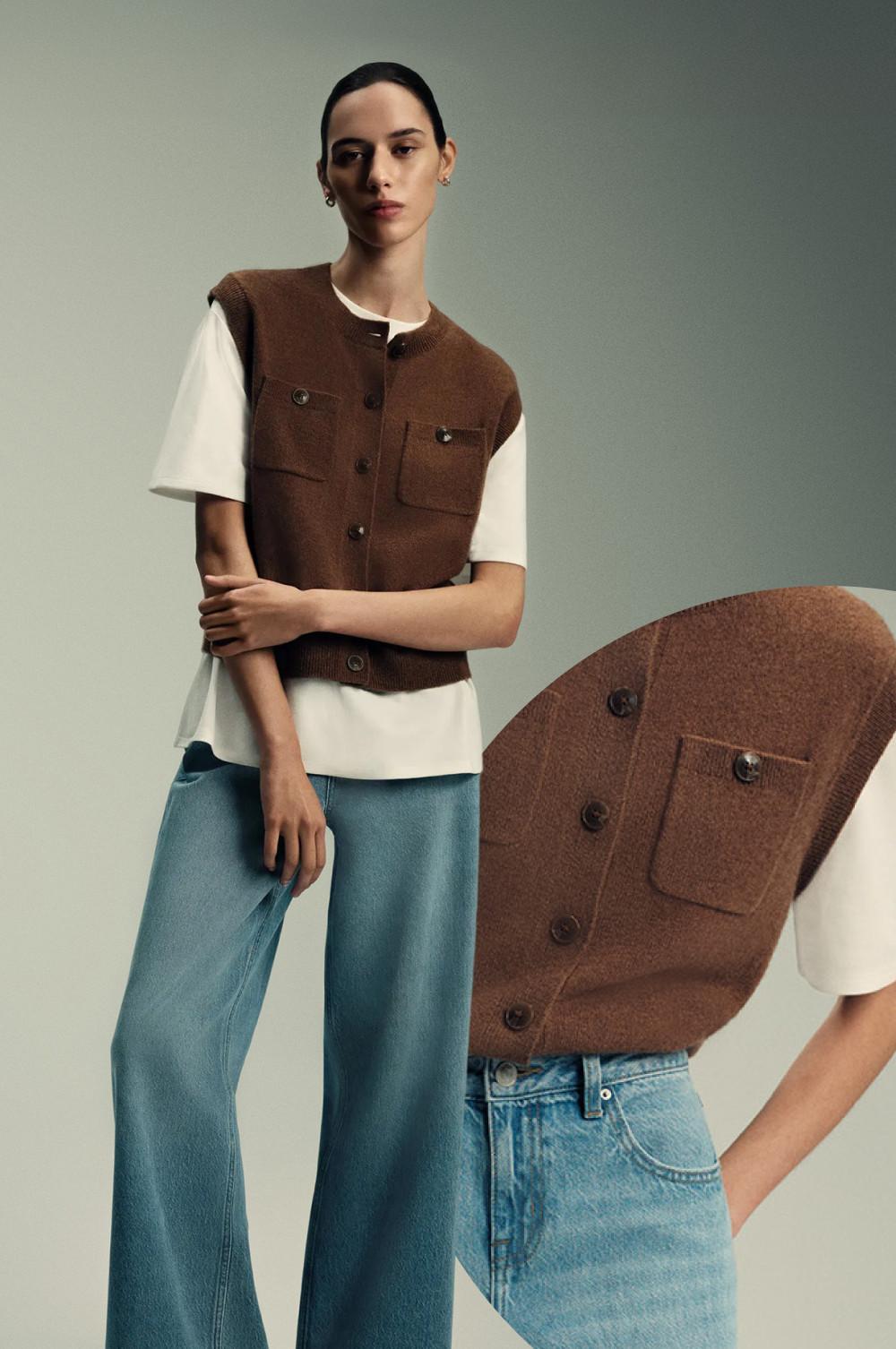 Chaleco de punto marrón con botones sobre una camiseta blanca y vaqueros azul claro de pernera ancha en un entorno minimalista.